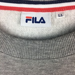 Op de afbeelding: Grijs sweatshirt met een wit Fila-logo en een rood-wit-blauwe streep aan de bovenkant. Het label zegt "LL".