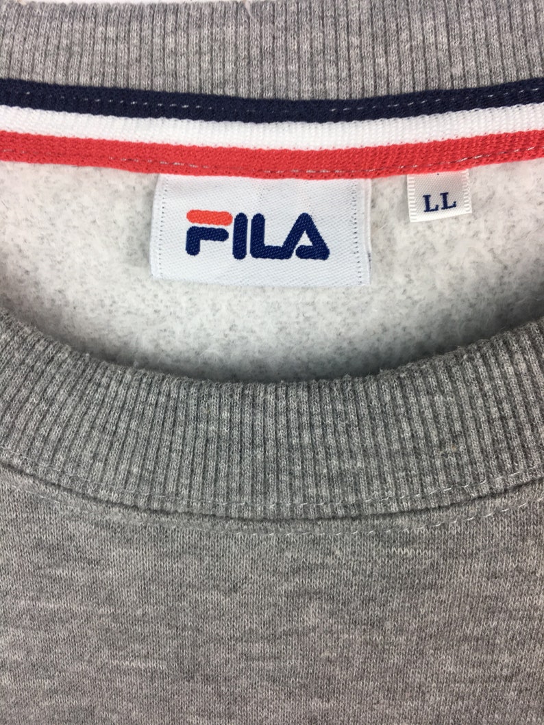 Op de afbeelding: Grijs sweatshirt met een wit Fila-logo en een rood-wit-blauwe streep aan de bovenkant. Het label zegt "LL".
