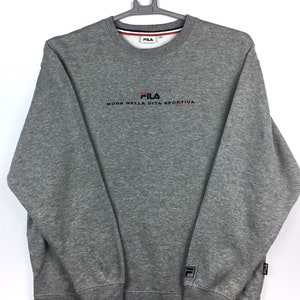 Op de afbeelding: Grijs sweatshirt met een Fila-logo en de tekst "Moda Nella Vita Sportiva" in rood en blauw. Het sweatshirt heeft een ronde hals en lange mouwen.