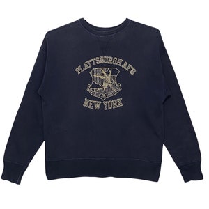 Może przedstawiać: Granatowa bluza z haftowanym złotym logo z napisem "Plattsburgh AFB" i "Strategic Air Command" oraz grafiką samolotu. Złotym haftem wykonano również napis "New York".