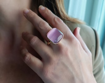 May include: A gold ring with a square, light pink gemstone.