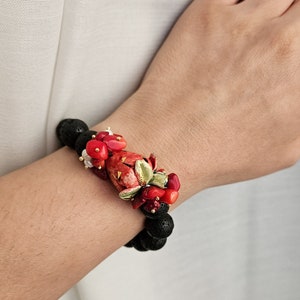 May include: A black lava rock bracelet with red coral and a red and gold ceramic flower charm.