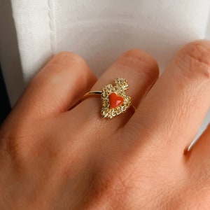 Peut inclure: Une bague en or avec un motif en forme de cœur rouge. La bague est ornée de détails filigranés complexes.