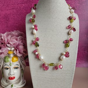 Può includere: Una delicata collana a catena dorata con perline di pietre preziose rosa e verdi e perle bianche. La collana è esposta su un manichino rivestito in tessuto.