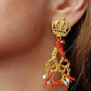 May include: Gold earrings with a crown design and red coral and white pearl accents.