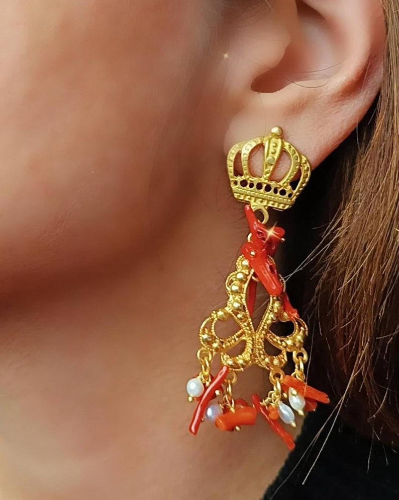 May include: Gold earrings with a crown design and red coral and white pearl accents.