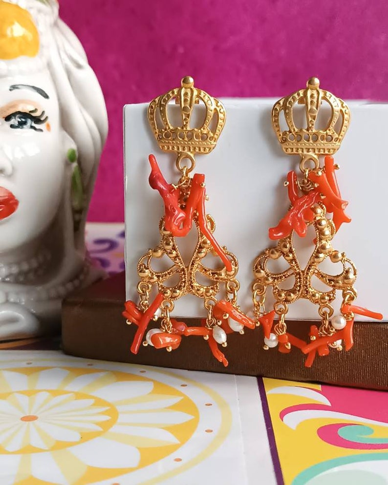 May include: Gold crown dangle earrings with red coral and white pearl accents.