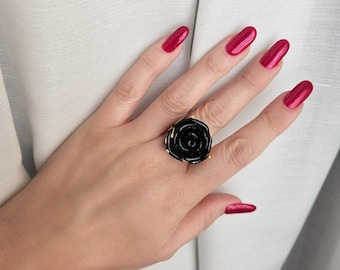 May include: A black rose ring with gold accents. The ring is worn on a hand with red nail polish.
