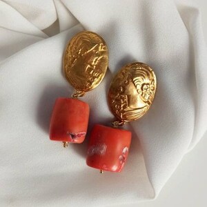Pu&ograve; includere: Orecchini dorati con un designo floreale dettagliato e perline color corallo.