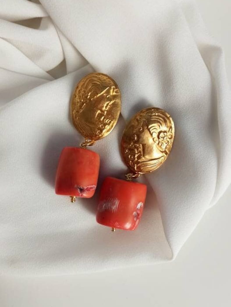 Pu&ograve; includere: Orecchini dorati con un designo floreale dettagliato e perline color corallo.