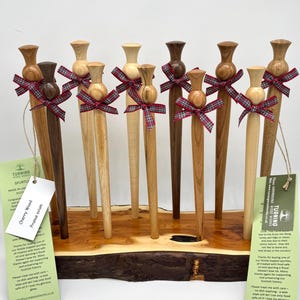 以下が含まれることがあります： 赤と黒の格子縞のリボンが付いた木製のチェリーウッドスパチュラ10本を展示しています。スパチュラは木製の板の上に置かれています。タグには「チェリーウッド Prunus avium」と書いてあります。