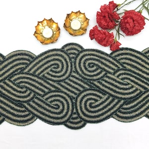 Puede incluir: Un camino de mesa de cuentas verde y dorado con un patrón de espiral. El camino de mesa está hecho de pequeñas cuentas que se tejen juntas para crear un diseño único y elegante.