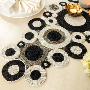 Peut inclure: Un chemin de table en perles noires et blanches avec un motif circulaire. Le chemin de table est fait de petites perles cousues ensemble pour créer un design unique.