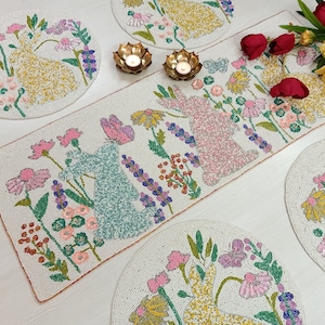 May include: A set of four white beaded placemats with floral and bunny designs. The placemats feature a variety of colours, including pink, blue, yellow, and green. The placemats are perfect for adding a touch of elegance to any dining table.