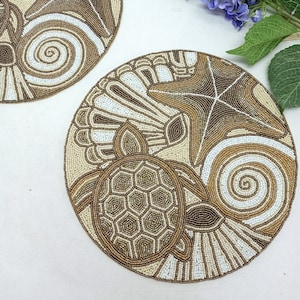 Pode incluir: Dois tapetes redondos de contas em tons bege e castanho. Os tapetes apresentam um design de cavalo-marinho, estrela do mar e tartaruga.