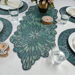 May include: A teal blue beaded table runner with a floral design. The runner is on a white tablecloth with place settings and candles.