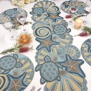 Może przedstawiać: Błękitny i brązowy, koralikowy bieżnik na stół z motywem morskim. Bieżnik przedstawia żółwie morskie, rozgwiazdy i muszle.