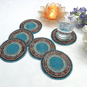 以下が含まれることがあります： 円形のデザインのターコイズブルーとブラウンのビーズコースター6個セット。コースターはビーズでできており、隆起したパターンがあります。