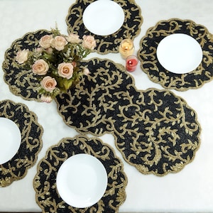 May include: Set of six black and gold beaded placemats with intricate floral designs. The placemats are round and have a scalloped edge.