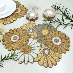 Pode incluir: Um conjunto de quatro tapetes de contas com um design floral em contas amarelas, brancas e marrons. Os tapetes são perfeitos para adicionar um toque de elegância a qualquer mesa de jantar.