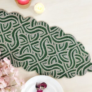 May include: A green beaded table runner with a geometric pattern. The runner has a scalloped edge and is made of small, round beads.