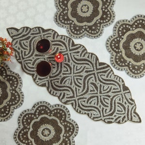 Peut inclure: Un ensemble de quatre sets de table en perles de couleur marron et argent. Les sets de table présentent un motif floral avec un cercle central et un bord festonné. Les sets de table sont disposés sur une surface blanche avec un chemin de table au centre.