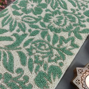 May include: A green and white beaded table runner with a floral pattern. The runner is made of small beads that are sewn together to create a raised design.