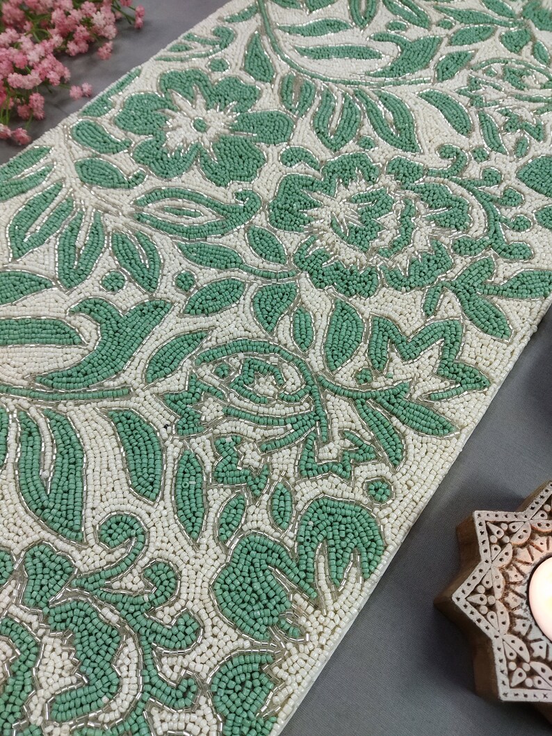 May include: A green and white beaded table runner with a floral pattern. The runner is made of small beads that are sewn together to create a raised design.