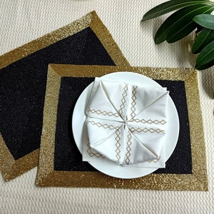 Peut inclure: Deux sets de table en perles noires et dorées avec une serviette blanche pliée au centre du plus grand set de table.