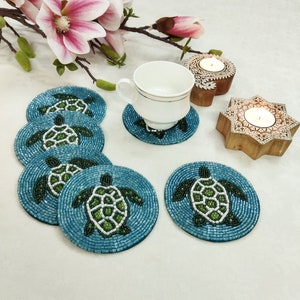 May include: Set of six blue and green beaded coasters featuring a turtle design. The coasters are round and have a white background with a blue border.