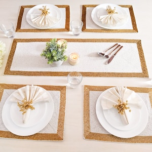 Puede incluir: Un juego de seis manteles individuales de cuentas blancas con ribete dorado. Cada mantel individual tiene una servilleta blanca con un anillo de servilleta dorado y un plato blanco con un borde dorado.