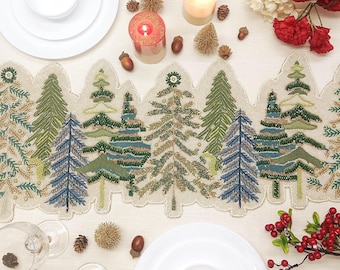 May include: A beige table runner featuring an embroidered forest scene with various evergreen trees in shades of green, blue, and gold. The runner has a scalloped edge and detailed beadwork throughout the tree designs.