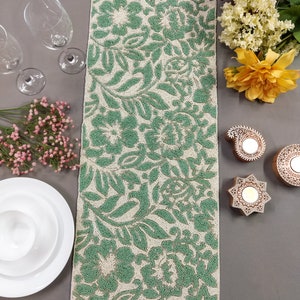 May include: A green and white beaded table runner with a floral pattern. The runner is made of small beads that are sewn together to create a raised design.