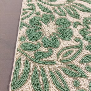 May include: A green and white beaded table runner with a floral design. The runner is made of small, round beads that are sewn together to create a intricate pattern.