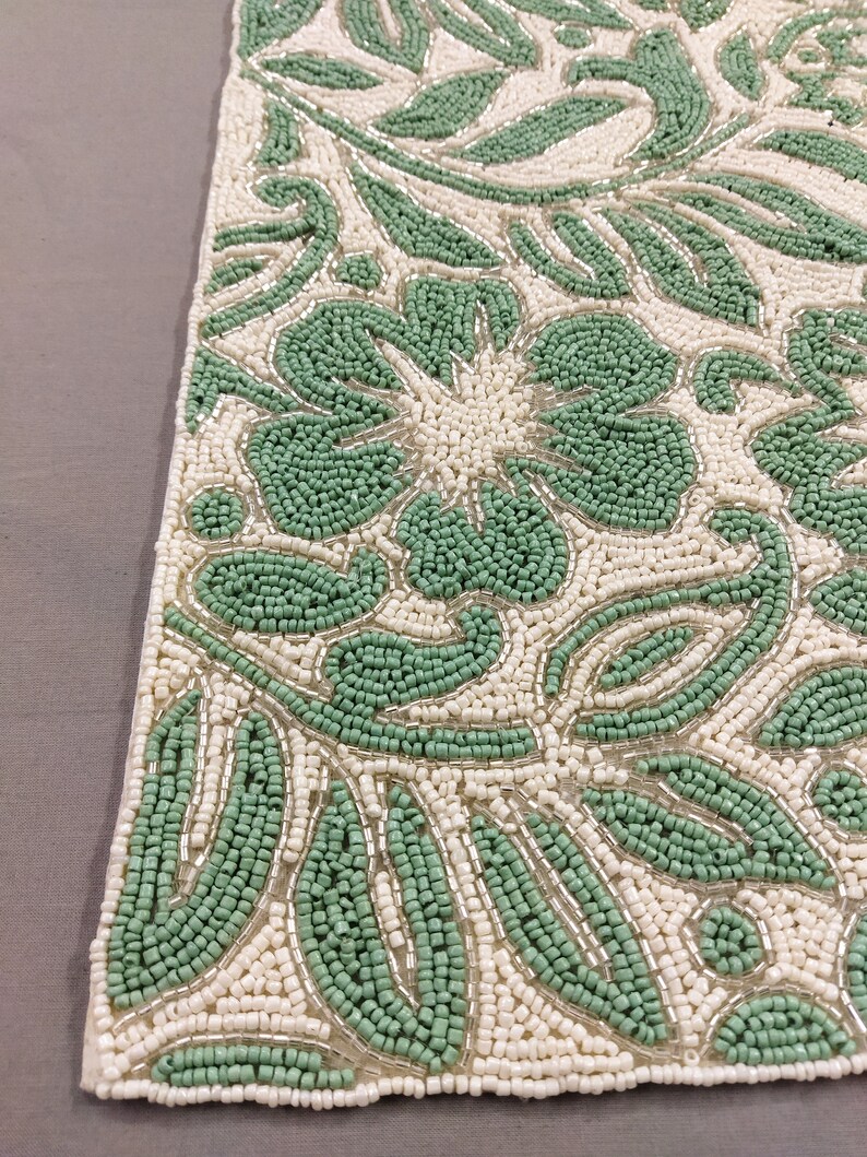 May include: A green and white beaded table runner with a floral design. The runner is made of small, round beads that are sewn together to create a intricate pattern.
