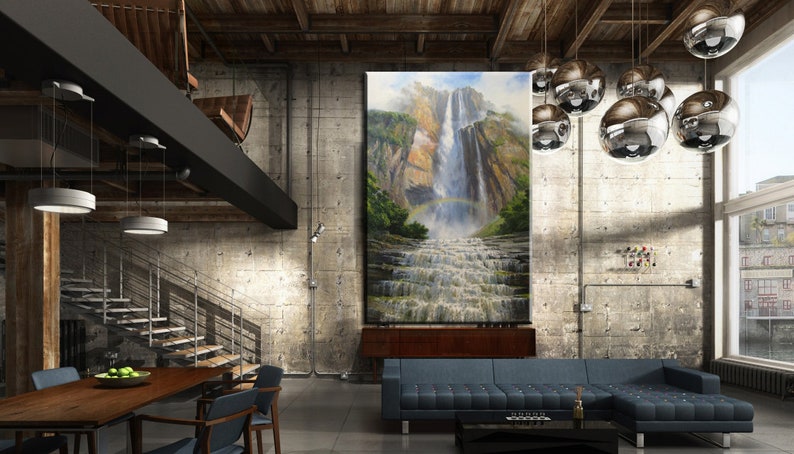 May include: A large, framed painting of a waterfall in a lush green forest hangs on a concrete wall in a modern loft living room. The room features a large sectional sofa, a wooden coffee table, and a dining table with chairs. The room has a rustic industrial design with exposed beams and pipes.