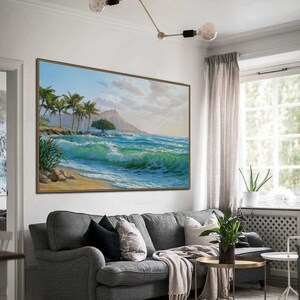 Puede incluir: Una pintura que representa una escena de playa tropical con palmeras, una monta&ntilde;a en la distancia y olas azules rompiendo en la orilla. La pintura est&aacute; enmarcada y colgada en una pared de una sala de estar.