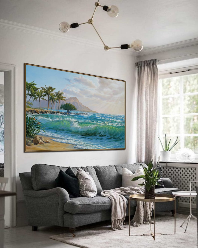 Puede incluir: Una pintura que representa una escena de playa tropical con palmeras, una monta&ntilde;a en la distancia y olas azules rompiendo en la orilla. La pintura est&aacute; enmarcada y colgada en una pared de una sala de estar.