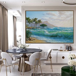 Puede incluir: Una pintura de una escena de playa tropical con palmeras, una monta&ntilde;a en la distancia y olas azules del oc&eacute;ano rompiendo en la orilla. La pintura est&aacute; enmarcada y colgada en una pared en un comedor con una mesa redonda y sillas.