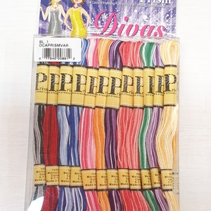 Puede incluir: Un paquete de 16 madejas de hilo de bordar en varios colores. El hilo está etiquetado como "Prism Divas" y "Six Strand Flax". El paquete también incluye el texto "The Colors of Friendship".