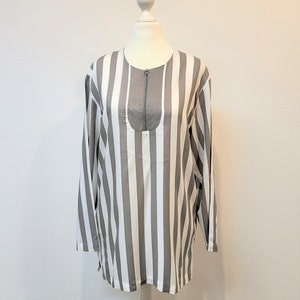 Puede incluir: Una camisa de manga larga a rayas grises y blancas con cuello de cremallera.