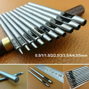 May include: Set of ten silver leather hole punch tools with different sizes ranging from 0.5 mm to 5 mm. The tools are laid out on a brown surface with a ruler and a wooden handle in the background.
