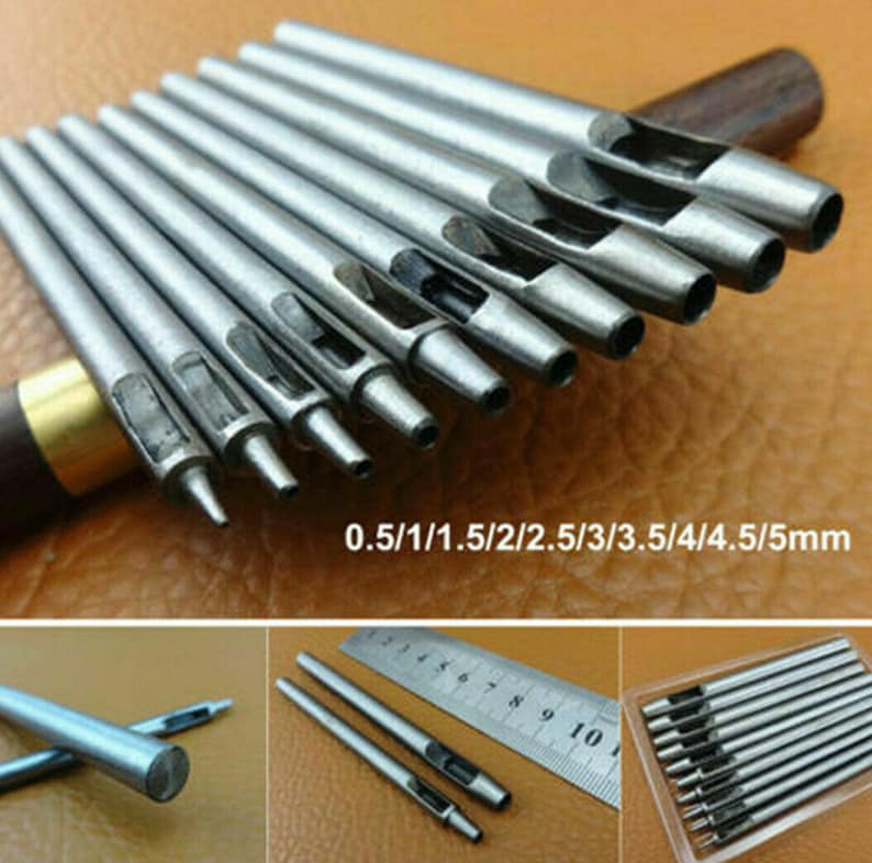May include: Set of ten silver leather hole punch tools with different sizes ranging from 0.5 mm to 5 mm. The tools are laid out on a brown surface with a ruler and a wooden handle in the background.