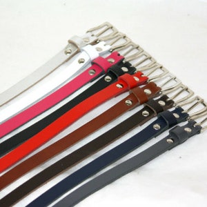 May include: A collection of leather belts in various colours, including white, pink, red, brown, black, navy and grey. The belts have silver buckles and are arranged in a fan shape.