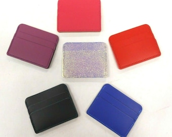 May include: Six different colored leather card holders. The card holders are arranged in a circle on a white background. The colors are pink, purple, silver, red, black, and blue.