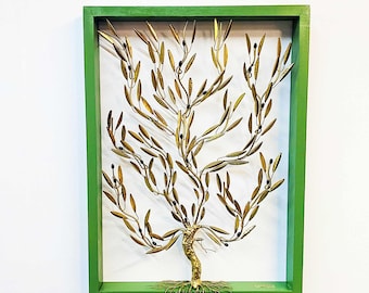 Op de afbeelding: Een gouden metalen olijfboom sculptuur met een groene lijst. De boom heeft een gedraaide stam en veel takken met bladeren en kleine zwarte olijven. De boom is geworteld in een basis van draad.