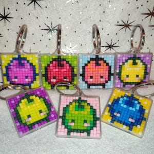 May include: Seven colourful pixel art keychains featuring different characters. Each keychain is made of plastic beads and has a silver metal ring.