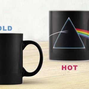 Puede incluir: Una taza de cerámica negra con un diseño sensible al calor. Cuando está fría, la taza es negra. Cuando está caliente, la taza revela un triángulo negro con un prisma de arcoíris, un diseño inspirado en la portada del álbum "Dark Side of the Moon" de Pink Floyd.