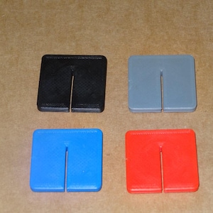 Peut inclure: Quatre carrés en plastique avec une fente verticale au centre. Les carrés sont noir, gris, bleu et rouge.