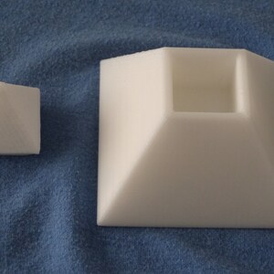 May include: Two white foam pyramid shapes. The smaller pyramid is solid, while the larger pyramid has a square opening in the top.